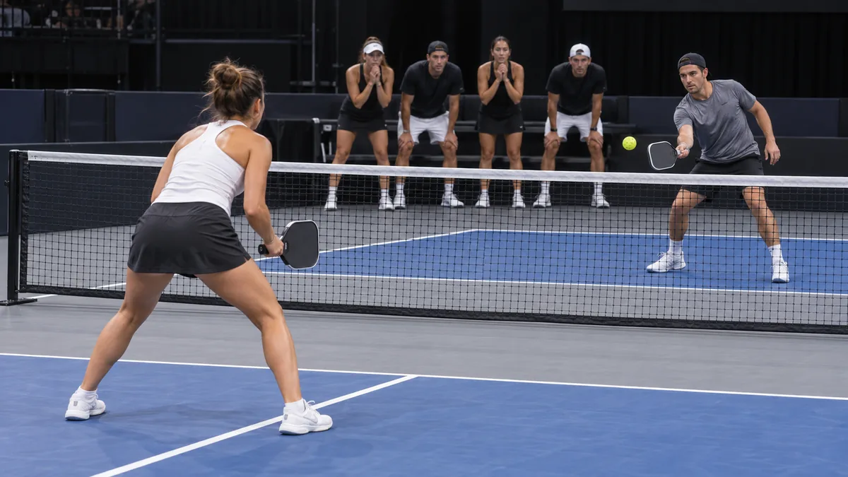 チームメートが見守る中でシングルスのラリーを戦う男女選手